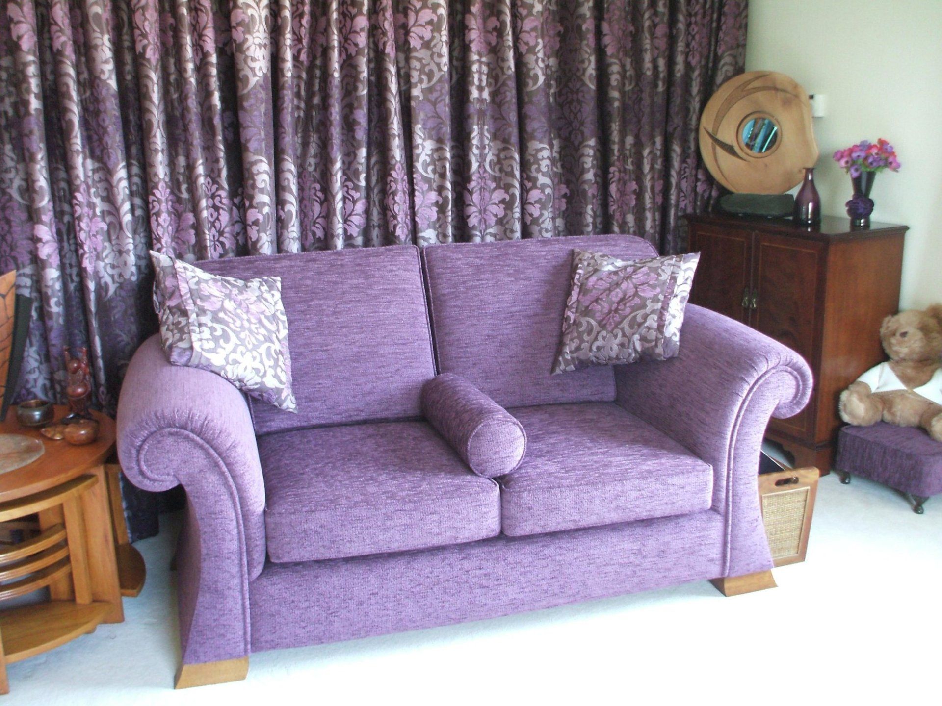 Purple two-seat sofa in a living room with curtains and cushions