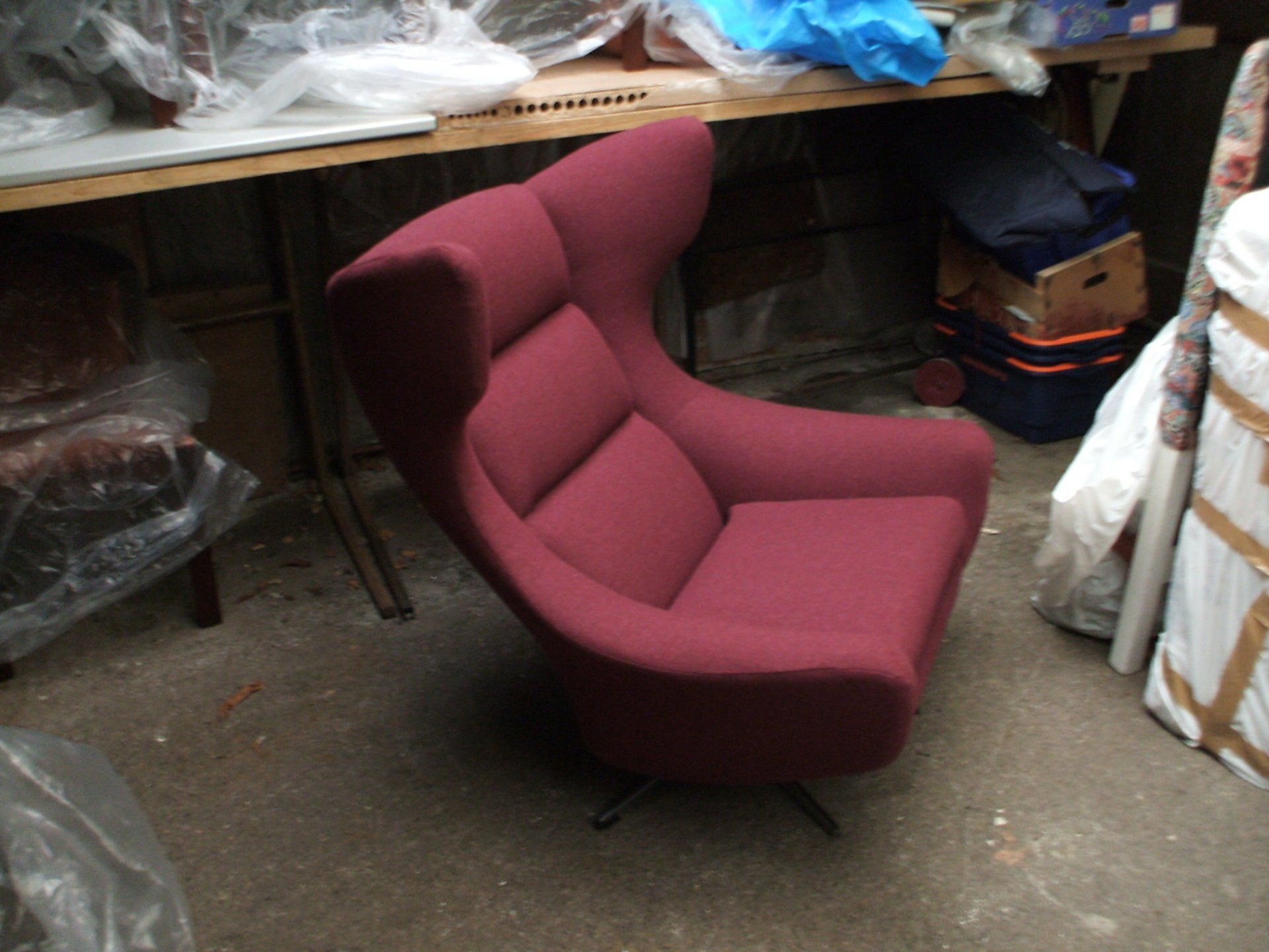 Curved magenta lounge chair in the workshop with rolls of fabric behind