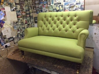 Green button-back settee in the workshop with fabric samples on the wall